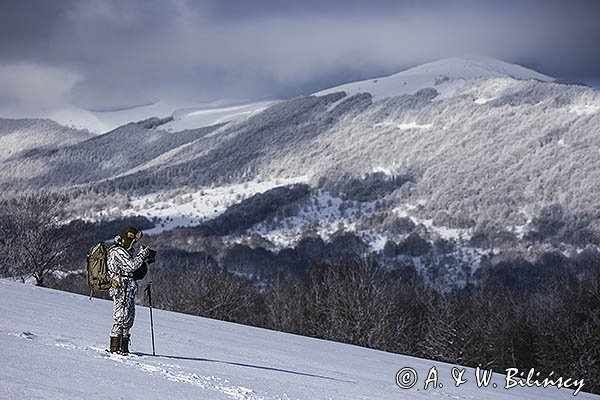 Zima, fotograf przyrody w stroju maskującym na rakietach śnieżnych