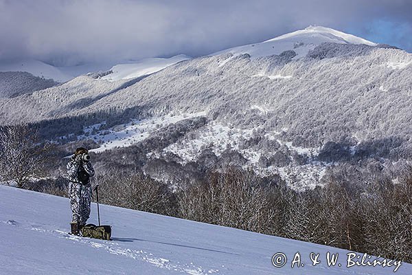 Zima, fotograf przyrody w stroju maskującym na rakietach śnieżnych